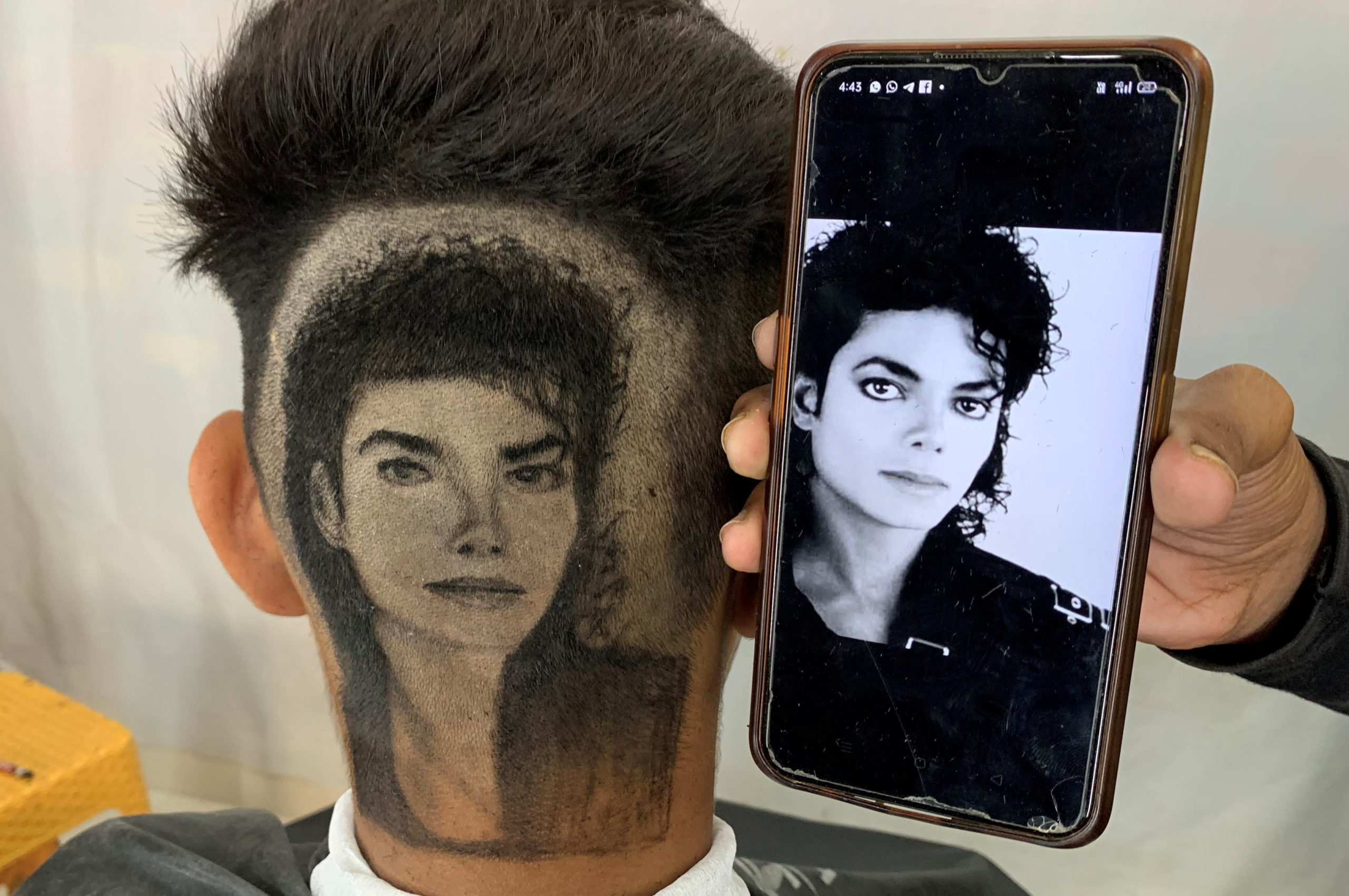 Gurwinder Singh Sidhu, a barber, displays a photo of Michael Jackson next to a customer after he made a hair tattoo of the pop star in the customer’s hair inside his shop in Dabwali town, in the northern state of Punjab, India